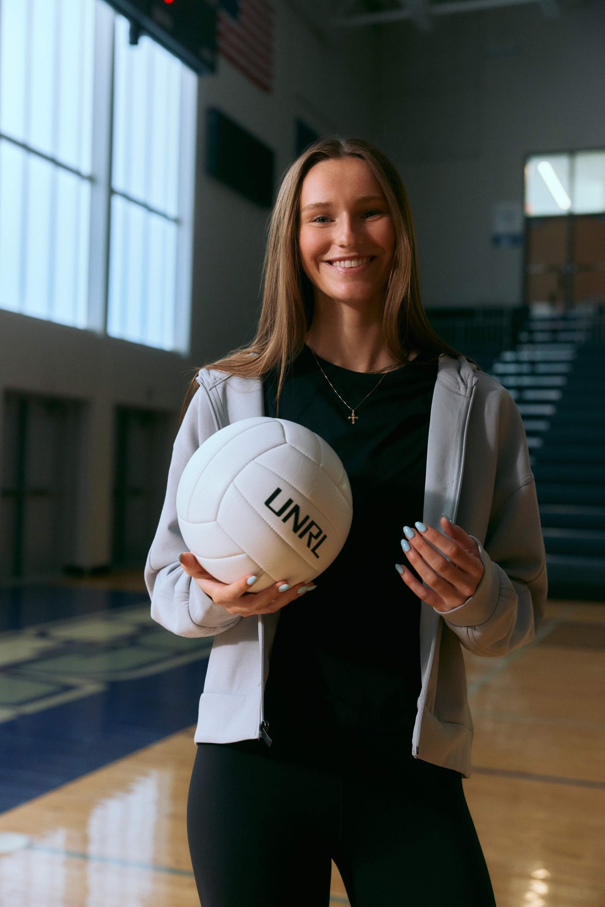 Woman holding a white volleyball with 'UNR' branding in an indoor gym.