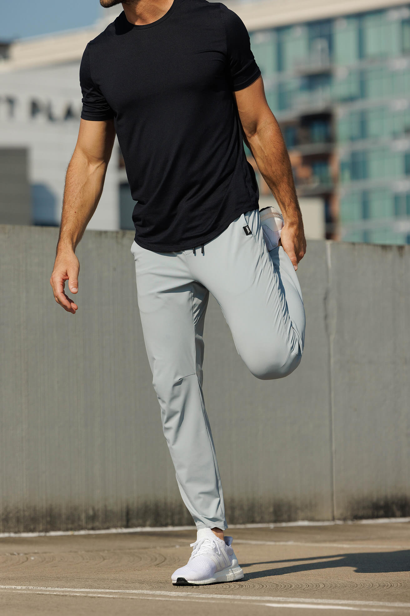 Person wearing a black t-shirt, gray pants, and white sneakers on a city street.