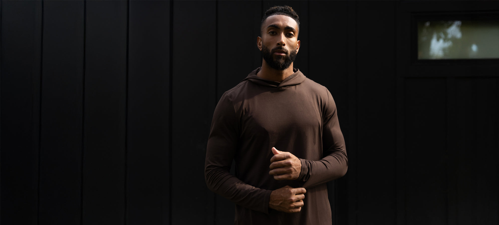 Man wearing a brown hoodie standing against a dark background